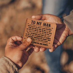 A close-up of two hands holding a personalized genuine leather bifold wallet engraved with a heartfelt message expressing love and inspiration for a husband or boyfriend.