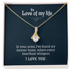 Gold chain necklace with a delicate ribbon-shaped pendant adorned with a sparkling clear stone, displayed inside a gift box with a romantic message for a loved one.