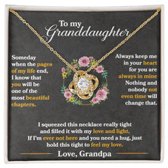 Gold love knot necklace with sparkling cubic zirconia on a chain, displayed on a black card with a heartfelt message to a granddaughter from grandpa surrounded by pink flowers.