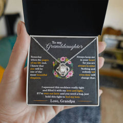 Hand holding an open black gift box containing a silver love knot necklace with cubic zirconia, displayed against a heartfelt printed message to a granddaughter from her grandpa.