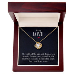 Gold-tone love knot necklace with a sparkling cubic zirconia center, displayed in a dark wood gift box with a heartfelt message, perfect for sentimental gifts.