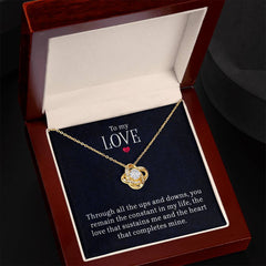 Gold love knot necklace with a sparkling cubic zirconia pendant displayed in an elegant wooden gift box, accompanied by a heartfelt romantic message.