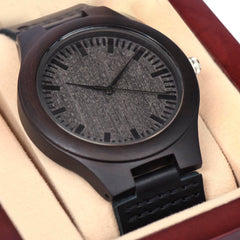 Close-up of a dark wooden wristwatch with a textured face and minimalist black hour markers, presented in a cushioned gift box, ideal as a sentimental gift.