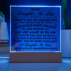 Illuminated acrylic plaque with heartfelt message for a daughter-in-law, glowing blue on a wooden light-up base, placed on a table with a plant nearby.