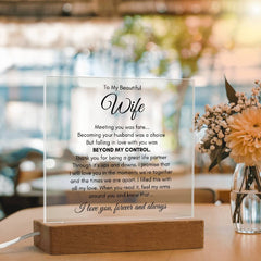 Transparent acrylic plaque with a heartfelt message to a wife, displayed on a wooden base with soft natural light and flowers in the background, ideal for a sentimental gift.