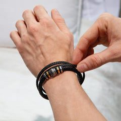 Close-up of a man's wrist wearing a black braided leather bracelet with metal accents, styled as a meaningful gift symbolizing love and encouragement.