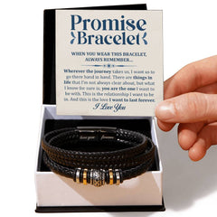 Hand holding a promise card with a heartfelt message above a black braided leather bracelet featuring gold and silver accents, presented in an open gift box.