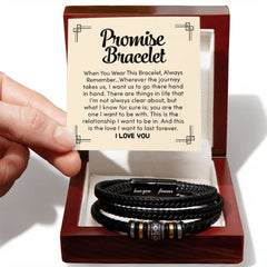 Hand holding a card with a heartfelt promise message above a black braided leather bracelet engraved with "love you" and "forever" inside a polished wooden gift box.