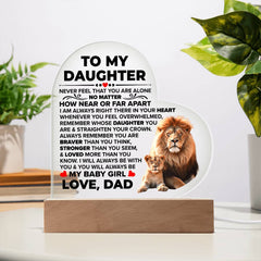 Clear acrylic heart plaque with an inspirational message from father to daughter, featuring a lion and cub illustration, displayed on a wooden base with indoor plants nearby.