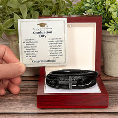 Handcrafted men's black braided leather bracelet with a stainless steel cross, displayed in a wooden gift box alongside a heartfelt graduation message card.