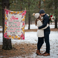 Couple embracing outdoors in winter near a tree with a colorful floral coral fleece blanket hanging on a clothesline, featuring a heartfelt message from a son to his mom.