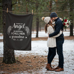 Dark coral fleece blanket hanging on a clothesline outdoors with white text reading "I have an angel in heaven I call her grandma," next to a couple embracing in winter clothing in a snowy forest setting.