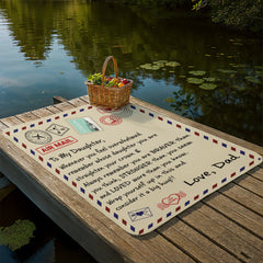 Sherpa fleece blanket designed like a vintage airmail envelope, draped on a wooden dock by a calm lake, featuring a heartfelt message from a dad to his daughter.