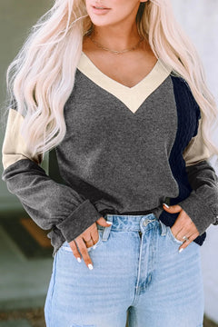 Woman wearing a cozy long sleeve black and cream colorblock knit top with a V-neck paired with light blue high-waisted jeans, styled with delicate jewelry.