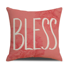 Coral pink decorative throw pillow with soft velvet texture and large white letters spelling "BLESS," featuring subtle floral patterns in the background.