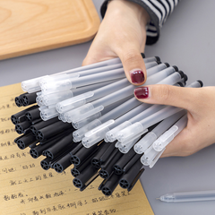 Hand holding a bundle of pens with black barrels and translucent caps, resting over a sheet of handwritten text on a wooden surface.