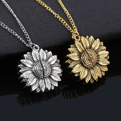 Pair of sunflower-shaped locket necklaces in silver and gold tones with intricate petal details, resting on a black fabric background.