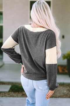 Woman wearing a long sleeve black and beige colorblock knit top with a V-neck, paired with light blue distressed jeans, standing outdoors with her back facing the camera.