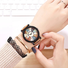Woman wearing a vintage-inspired wristwatch with a multicolor dial and retro leather strap, paired with delicate bracelets, resting hands on a wooden surface near a keyboard.