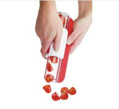 Hands using a red and white slicer to cut cherry tomatoes into even pieces, demonstrating precise and easy slicing for kitchen preparation.