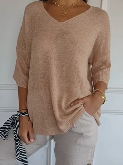 Woman wearing a soft beige V-neck knit sweater with three-quarter sleeves, paired with light-colored pants and layered gold necklaces, styled casually with bracelets and a zebra scarf tied to her wrist.