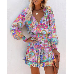 Woman wearing a colorful patchwork dress with long puff sleeves and a ruffled hem, featuring floral and paisley prints, styled with layered necklaces and a clutch purse.