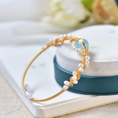 Delicate gold-plated wire bracelet featuring braided vintage style with natural baroque pearls and a light blue charm, perfect as a stylish gift for her.