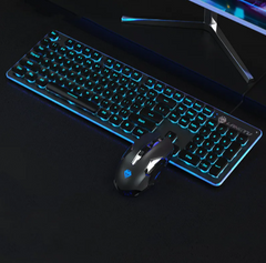 Black USB wired gaming keyboard with blue backlit keys and matching illuminated gaming mouse on a dark desk, positioned in front of a computer monitor.