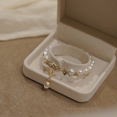 Elegant white pearl bracelet with gold chain and charm, displayed in a soft beige jewelry box, perfect as a luxury gift for special occasions.