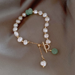 Elegant bracelet featuring irregular white freshwater pearls paired with natural green jade beads and gold accents, displayed on a soft brown fabric background.