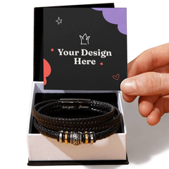 Black braided leather bracelet with engraved magnetic clasp and decorative gold and silver accents displayed in an open gift box with customizable design cover being lifted by hand